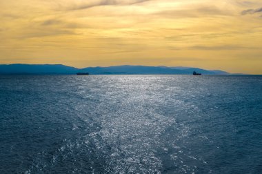 Koyu mavi deniz ve sarı günbatımı gökyüzü olan deniz manzarası. Koyu mavi denize karşı karanlık adalar üzerinde renkli gün batımı ve bulutlu gökyüzü. İzmit Körfezi yakınlarındaki Türkiye kıyılarının panoramik manzarası