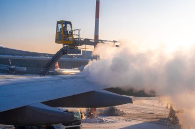 Moskova, Rusya - 12 Ocak 2022: Sheremetyevo Uluslararası Havaalanı. Bir uçak kanadının buzunu çözüyorum. Dondurma önleyici beyaz sıvı püskürtme işlemi kışın gündoğumunda havaalanında bir uçağın kanadının arka kısmında.