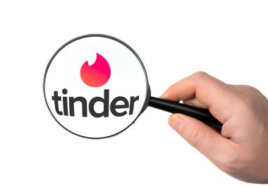 New York, ABD - 11 Ocak 2022: Büyüteç altında Tinder uygulaması logosu. Beyaz masanın üst görüntüsü. Tinder, parametrelerin konumlandırılmasına uygun olarak romantik randevular için tasarlanmış popüler bir araçtır.
