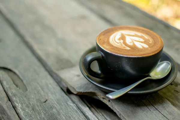 A cup of black coffee is placed on a brown wooden floor.