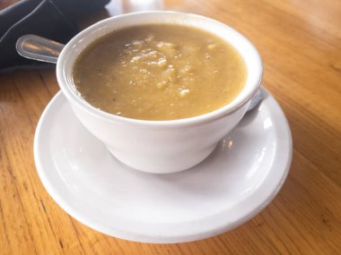 Bir fincan ezilmiş mercimek çorbası. Tahta bir yüzey üzerinde kaşıkla beyaz bir tabakta servis edilmiş..