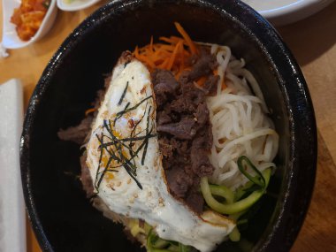 Tahta bir masada servis edilen beyaz bir kasede soğanlı, bezelyeli ve havuçlu yumurta çorbası.