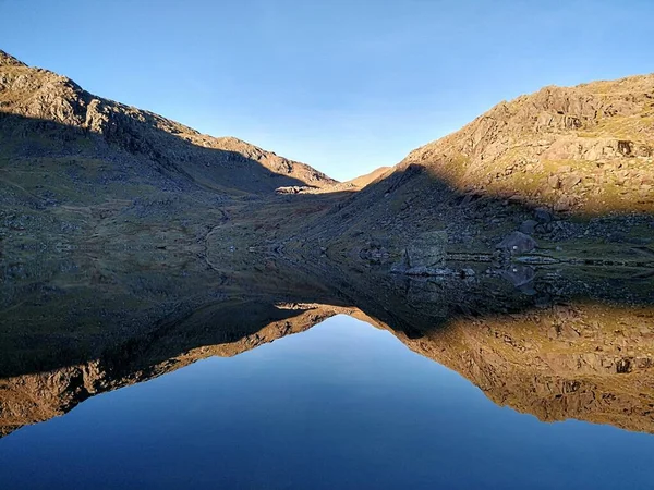 A view of a lake displaying a mirror image reflection of the mountains around the Old Man of Coniston in the Lake District