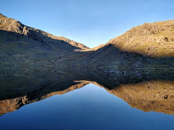 Lake District 'teki Coniston' un Yaşlı Adamı 'nın etrafındaki dağların ayna görüntüsünü gösteren bir göl manzarası.