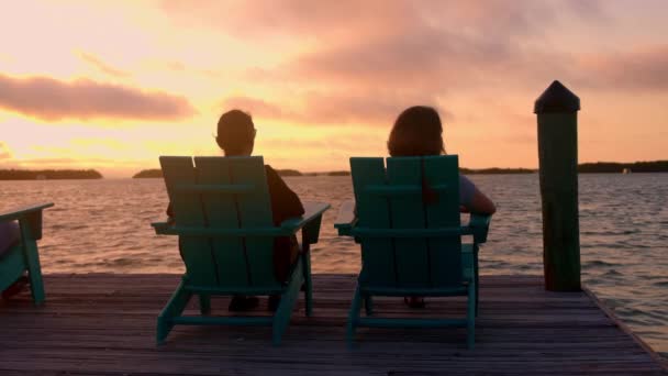 Duas mulheres sentam-se em uma cadeira de praia e desfrutam do pôr do sol — Vídeo de Stock