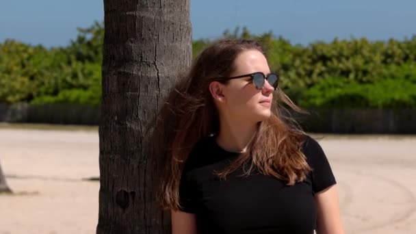 Miami Plajı 'nda palmiye ağacına yaslanan genç bir kadın. — Stok video