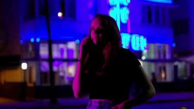 Gece Miami Plajı 'ndaki Renkli Okyanus Yolu' nda genç bir kadın neon ışıklarının altında bir telefon alıyor.