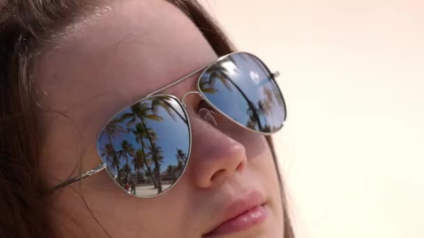 Close-up shot van een vrouw met een zonnebril op het strand onder palmbomen — Stockvideo