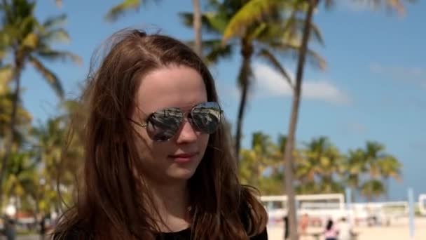 Close-up shot van een mooi meisje onder palmbomen op het strand — Stockvideo