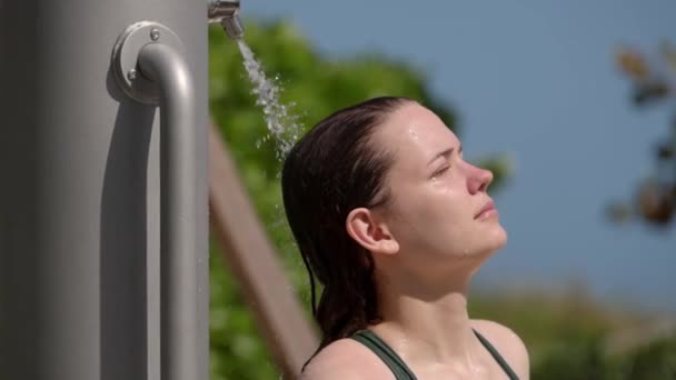 Молодая женщина принимает душ после принятия солнечных ванн на пляже — стоковое видео