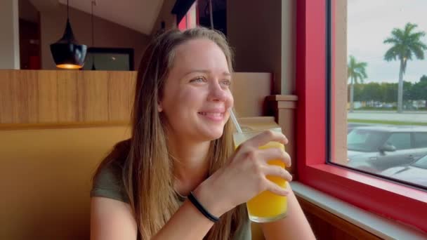 Νεαρή γυναίκα κάθεται σε ένα εστιατόριο και πίνει χυμό πορτοκάλι — Αρχείο Βίντεο