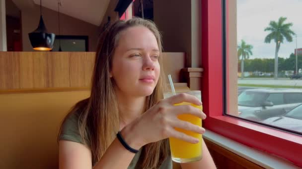 Ung kvinna sitter i en restaurang och dricker apelsinjuice — Stockvideo