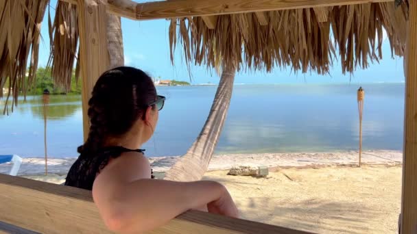 Paradise beach - Jonge vrouw zittend op een bankje genietend van de Caribische sfeer — Stockvideo