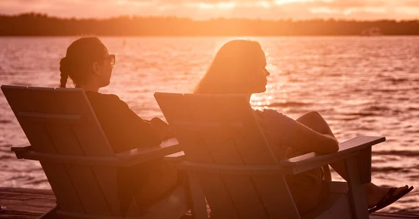 ビーチに座って水の上で夕日を楽しんでいる2人の若い女性 — ストック写真