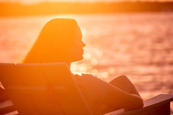 若い女性はビーチに座って海の上の夕日を楽しんでいます — ストック写真