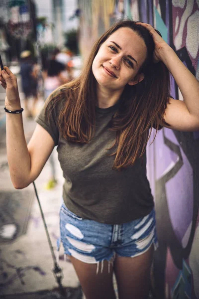 Νεαρή και όμορφη γυναίκα ακουμπά σε έναν πολύχρωμο τοίχο και ποζάρει για την κάμερα - τυπικό στυλ δρόμου — Φωτογραφία Αρχείου