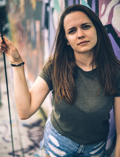 Mulher jovem e bonita se inclina contra uma parede colorida e posa para a câmera - estilo típico de rua — Fotografia de Stock