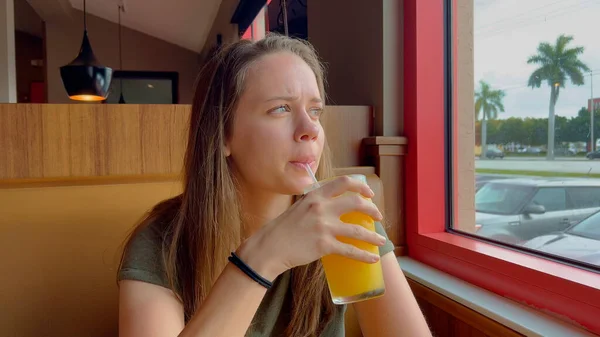 Молода жінка сидить в ресторані і п'є апельсиновий сік — стокове фото