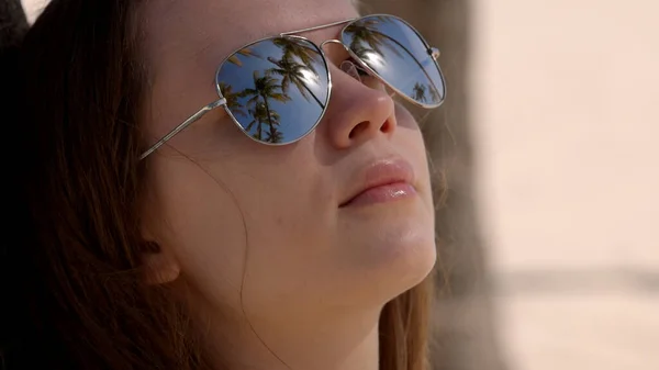 Foto ravvicinata di una donna che indossa occhiali da sole in spiaggia sotto le palme — Foto Stock