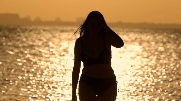 Silueta záběr krásné ženy při západu slunce výstřel proti zlatému oceánu vody — Stock fotografie
