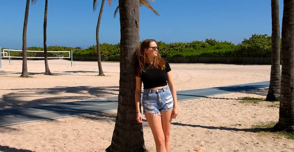 Jonge vrouw leunend tegen een palmboom op Miami Beach — Stockfoto