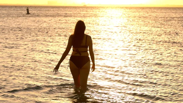 Silhouet shot van een mooie vrouw op zonsondergang schot tegen de gouden oceaan water — Stockfoto