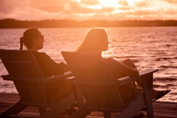 Twee jonge vrouwen zitten aan het strand en genieten van de zonsondergang boven het water — Stockfoto