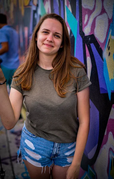 Mulher jovem e bonita se inclina contra uma parede colorida e posa para a câmera - estilo típico de rua — Fotografia de Stock