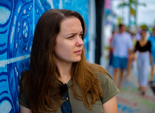 Mulher jovem e bonita se inclina contra uma parede colorida e posa para a câmera - estilo típico de rua — Fotografia de Stock