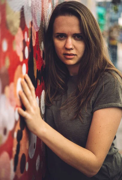 Mulher jovem e bonita se inclina contra uma parede colorida e posa para a câmera - estilo típico de rua — Fotografia de Stock