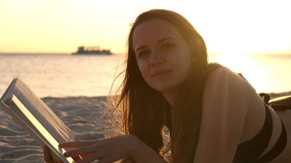 Giovane donna legge un libro mentre sdraiato sulla spiaggia al tramonto — Foto Stock