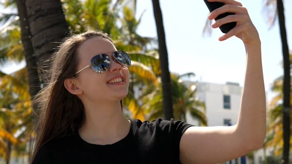 Mujer joven tomando una selfie bajo palmeras en la playa — Foto de Stock