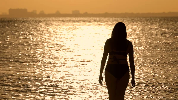 Silueta záběr krásné ženy při západu slunce výstřel proti zlatému oceánu vody — Stock fotografie