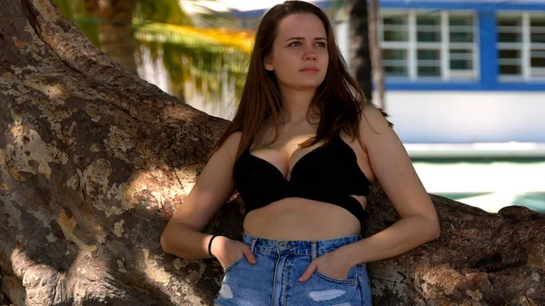 Joven mujer sexy apoyada en una palmera en la playa — Foto de Stock