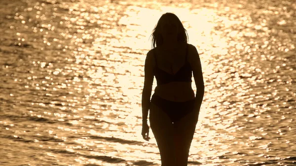 Silhueta tiro de uma bela mulher no pôr do sol tiro contra a água do oceano dourado — Fotografia de Stock