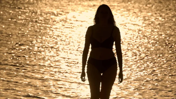 Silueta tiro de una hermosa mujer en la puesta del sol tiro contra el agua del océano de oro — Foto de Stock