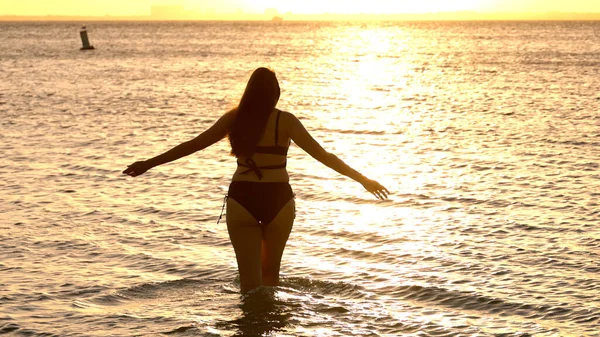 Silhouet shot van een mooie vrouw op zonsondergang schot tegen de gouden oceaan water — Stockfoto