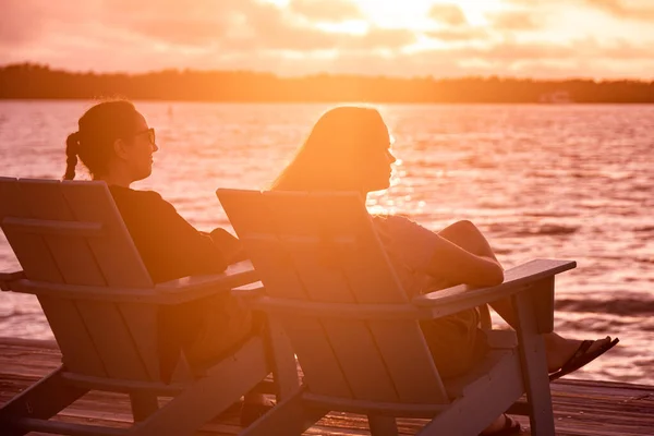 Twee jonge vrouwen zitten aan het strand en genieten van de zonsondergang boven het water — Stockfoto