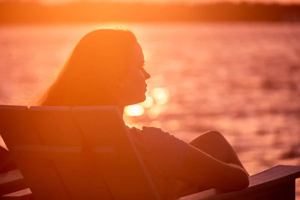 若い女性はビーチに座って海の上の夕日を楽しんでいます — ストック写真