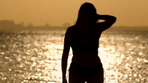 Silueta de una mujer contra el agua dorada del océano al atardecer — Vídeos de Stock