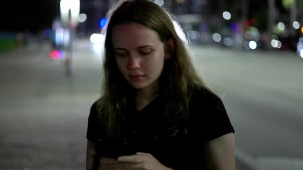 Młoda kobieta spacerująca nocą ulicą, pisząc sms-a na komórce. — Wideo stockowe