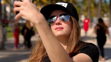 Genç bir kadın sahilde palmiye ağaçlarının altında selfie çekiyor.