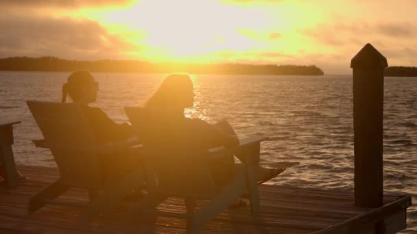 Duas mulheres sentam-se em uma cadeira de praia e desfrutam do pôr do sol — Vídeo de Stock