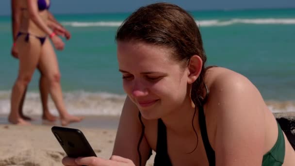 Mooie vrouw ontspant op het strand terwijl sms 'en met haar mobiele telefoon — Stockvideo