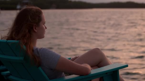 Mladá žena sedí na pláži a užívá si západ slunce — Stock video