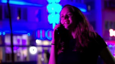 Gece Miami Plajı 'ndaki Renkli Okyanus Yolu' nda genç bir kadın neon ışıklarının altında bir telefon alıyor.