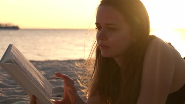 Genç kadın gün batımında sahilde yatarken bir kitap okuyor. — Stok video