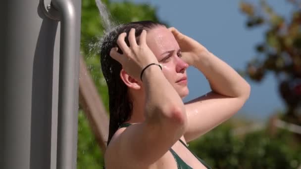 Jonge vrouw neemt een douche na zonnebaden op het strand — Stockvideo