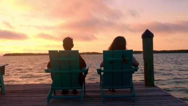Две женщины сидят в шезлонге и наслаждаются закатом — стоковое видео