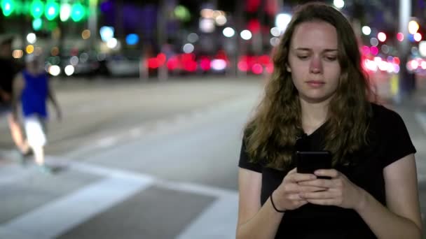 Geceleri sokakta yürürken cep telefonuyla mesajlaşan genç bir kadın. — Stok video